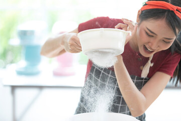 young woman housewife sifting flour from sieve in the kitchen