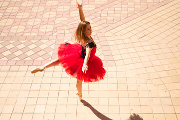 Classical ballet dancer dancing in the street. The dancer is wearing a red tutu and is performing a...