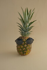 Pineapple, a tropical fruit with sunglasses on a beige background. Minimal concept.