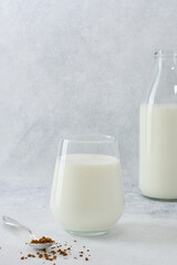 Ingredients to making coffee with milk. Instant coffee in spoon, a glass of milk and a bottle with milk on light grey background with copy space. 
