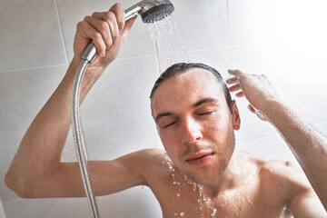 Portrait of young handsome man washes himself with shower gel, lathers head with shampoo in the...