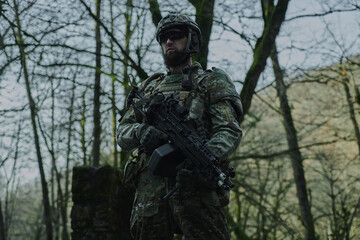 Portrait of airsoft player in professional equipment with machine gun in the forest. Soldier with weapons at war