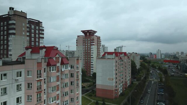 Flight over the city block in cloudy weather. Multi-storey buildings and trees with yellowed leaves in the suburbs. Gray sky shaded by clouds. Aerial photography.