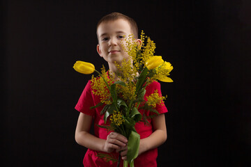 a boy with vitiligo in a red T-shirt with a bouquet of mimosa
