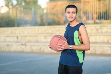 Young child holding a basketball. Happy teen with basket ball on basketball court at sunset.