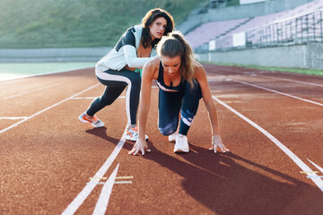 Young athlete exercises with personal trainer standing on start on stadium, then rushing forward,...