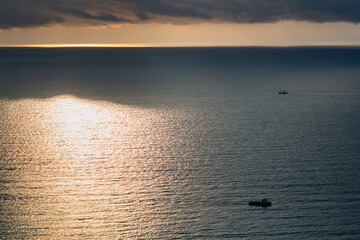 Two ships at sea at sunset on a cloudy rainy day under heavy dark clouds