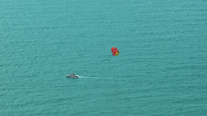 A parachutist above the sea surface flies behind a boat on a summer day, summer active recreation...