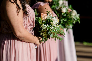 Beautiful bridesmaids in pink dresses holding  pink and white roses bouquets Close up bridesmaids bouquets hands Three bridesmaids standing and holding bouquets No faces captured
