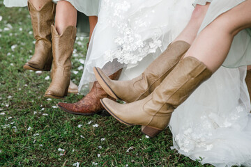 Bride and bridesmaids legs in cowboy boots on the foreground Bride's Wedding Cowboy Boots Details...