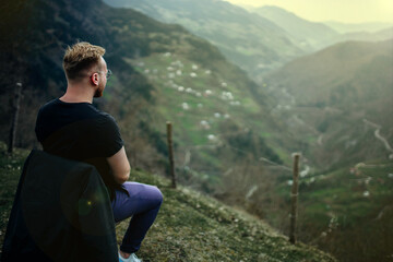 Naklejka na ściany i meble man sits in the mountains and looks into a beautiful valley enjoying nature, a journey of solitude.