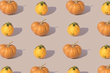 A pattern of orange pumpkins arranged on a pastel purple background. Minimal layout.