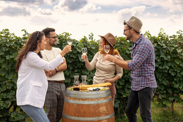 Four friends standing in vineyard with glasses of vine red and white drinking, relaxing and talk to each other in summer day.