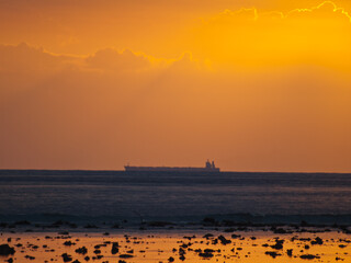 Cargo ship silhouette in the horizon line with sunset orange light