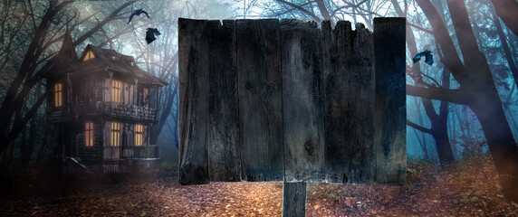 Rustic wooden notice board in front of foggy autumn forest and witch's house