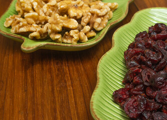 two green bowls full of cranberries and nuts on the wooden table
