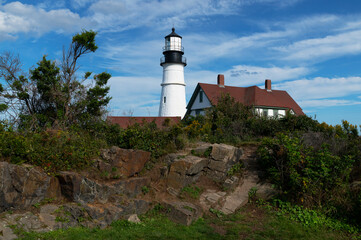 Fototapeta na wymiar Old Maine Lighthouse Sits on Rocky Ground Surrounded by Wildflowers.