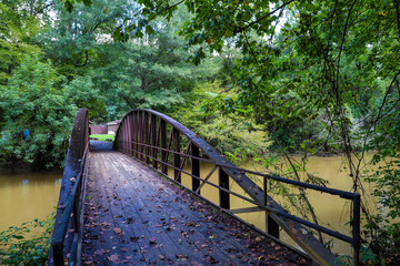 a shot of a rust colored iron bridge covered in fallen leaves over the brown waters of the...
