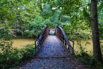 a shot of a rust colored iron bridge covered in fallen leaves over the brown waters of the...