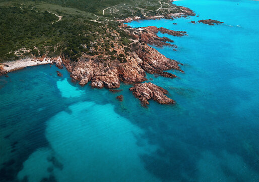 Aerial view of a reddish cliff surrounded by spectacular turquoise waters near Isola Rossa, Sardinia, Italy.