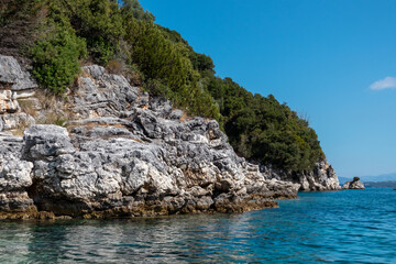 Fototapeta na wymiar Blue clear Ionian Sea water with scenic green rocky cliffs coast and bright sky. Nature of Lefkada island in Greece. Summer vacation idyllic travel destination