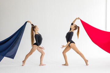 two slim artistic teenager girls in black leotards trains on white background with red fabric in...