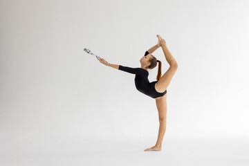 slim artistic teenager girl in black leotard trains on white background with clubs in her hands in...