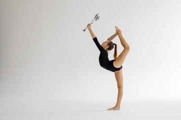 slim artistic teenager girl in black leotard trains on white background with clubs in her hands in...