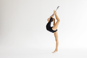 slim artistic teenager girl in black leotard trains on white background with clubs in her hands in rhythmic gymnastic exercise, children's professional sports - obrazy, fototapety, plakaty