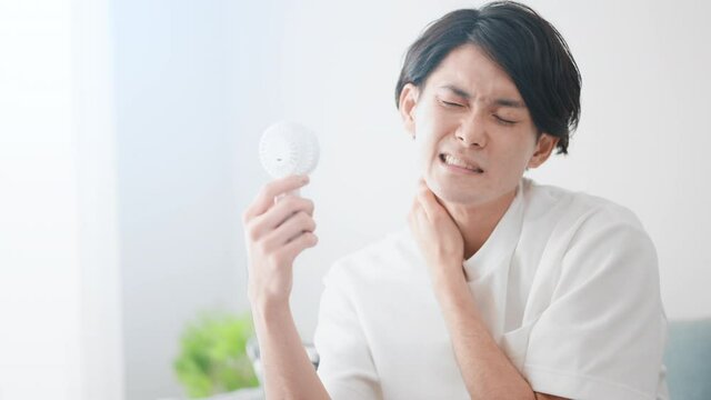 ハンディ扇風機で涼しんでいる男性