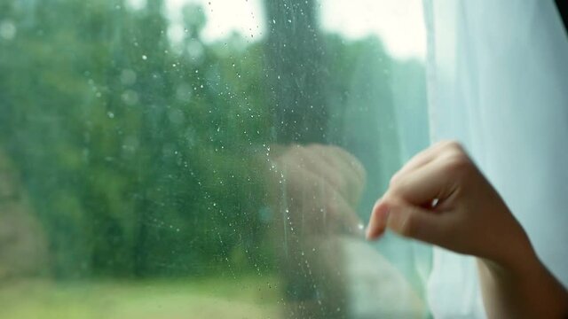 Bored Caucasian boy on a trip is bored sitting by the window with rain. A child on a train by the window through which raindrops are flowing. selective focus. child separation theme