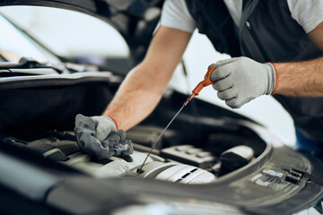 Close-up of auto repairman checks oil level during engine maintenance in workshop.