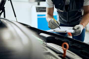 Close-up of mechanic writes data while examining car engine in workshop.