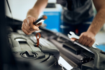 Close-up of mechanic examines car engine with lamp at auto repair shop.