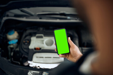 Close-up of mechanic uses smart phone while working at auto repair shop.