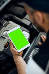 Close-up of auto mechanic uses touchpad while maintaining car engine in workshop.