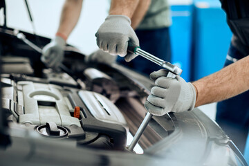 Close-up of auto mechanic uses wrench while working on car engine at repair shop.