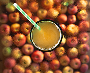 Natural, apple juice in a glass with a paper straw on a transparent glass background with drops of water and apples. Top view, flat lay, selective focus.
