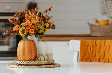 Still-life. Yellow, orange flowers in a vase, pumpkins and candles on a golden tray on a white...
