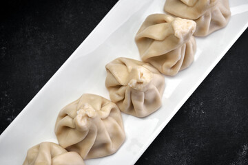Cooked Khinkali on a white plate on a dark background