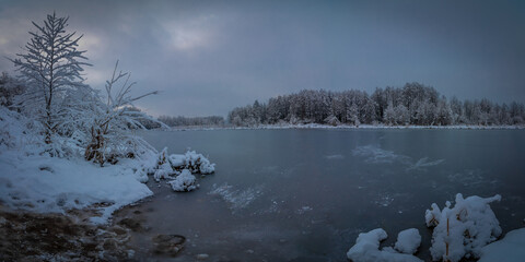 beautiful evening winter landscape. View from the snowy coast of a frozen river in cloudy weather