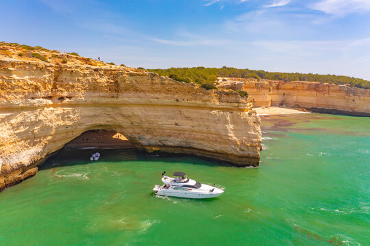 Aerial view of a yacht cruising by Praia da Corredoura beach near the cliffs of Benagil cave in Lagoa, Algarve, Portugal.