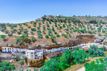 Calle de casas cueva construidas bajo la montaña cultivada con olivos desde Setenil de las Bodegas, Cádiz, Andalucía, España.