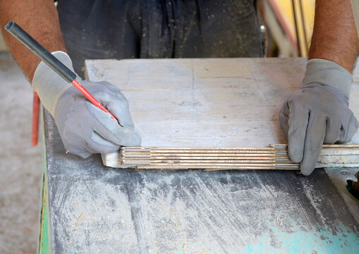 Construction carpenter measures and puts a pencil mark on a wooden board that needs to be cut with a circular saw on a construction site