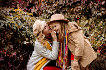 A young adult blonde mother with a 7-year-old daughter on a walk in the autumn park hug and laugh
