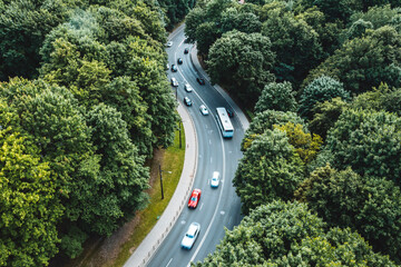 Aerial view of city traffic on curved road between green trees in Kaunas.