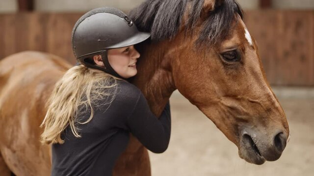 Woman In Riding Hat Stroking And Hugging Horse In Paddock