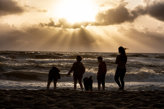 silhouettes of four teenagers and a dog on the beach of Jutland, Denmark. Looking into the wild surf of the ocean, sunset sky with  sun rays through the clouds
