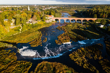 Venta Rapid waterfall, the widest waterfall in Europe and long red brick bridge in sunny autumn morning, Kuldiga, Latvia. Captured from above.
