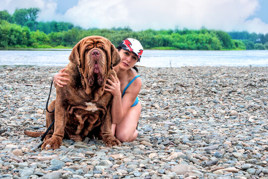 A woman hugging a big mastino napoletano dog at the river in summer.
